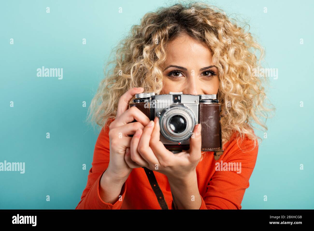 Bionda ragazza prende una ripresa con una macchina fotografica vintage. Sfondo ciano Foto Stock