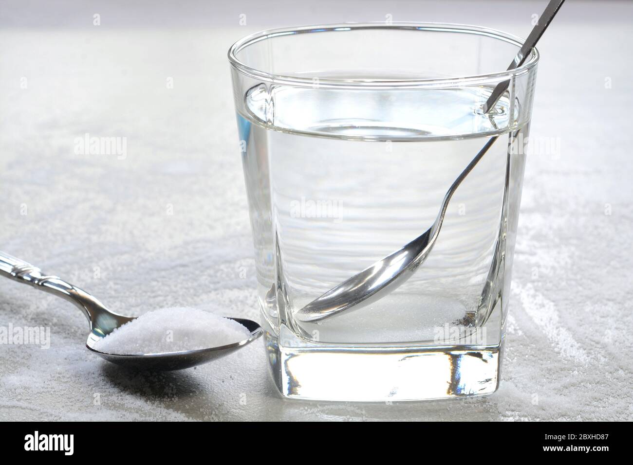 Salare l'acqua in una tazza di vetro e sale in un cucchiaino. Foto Stock