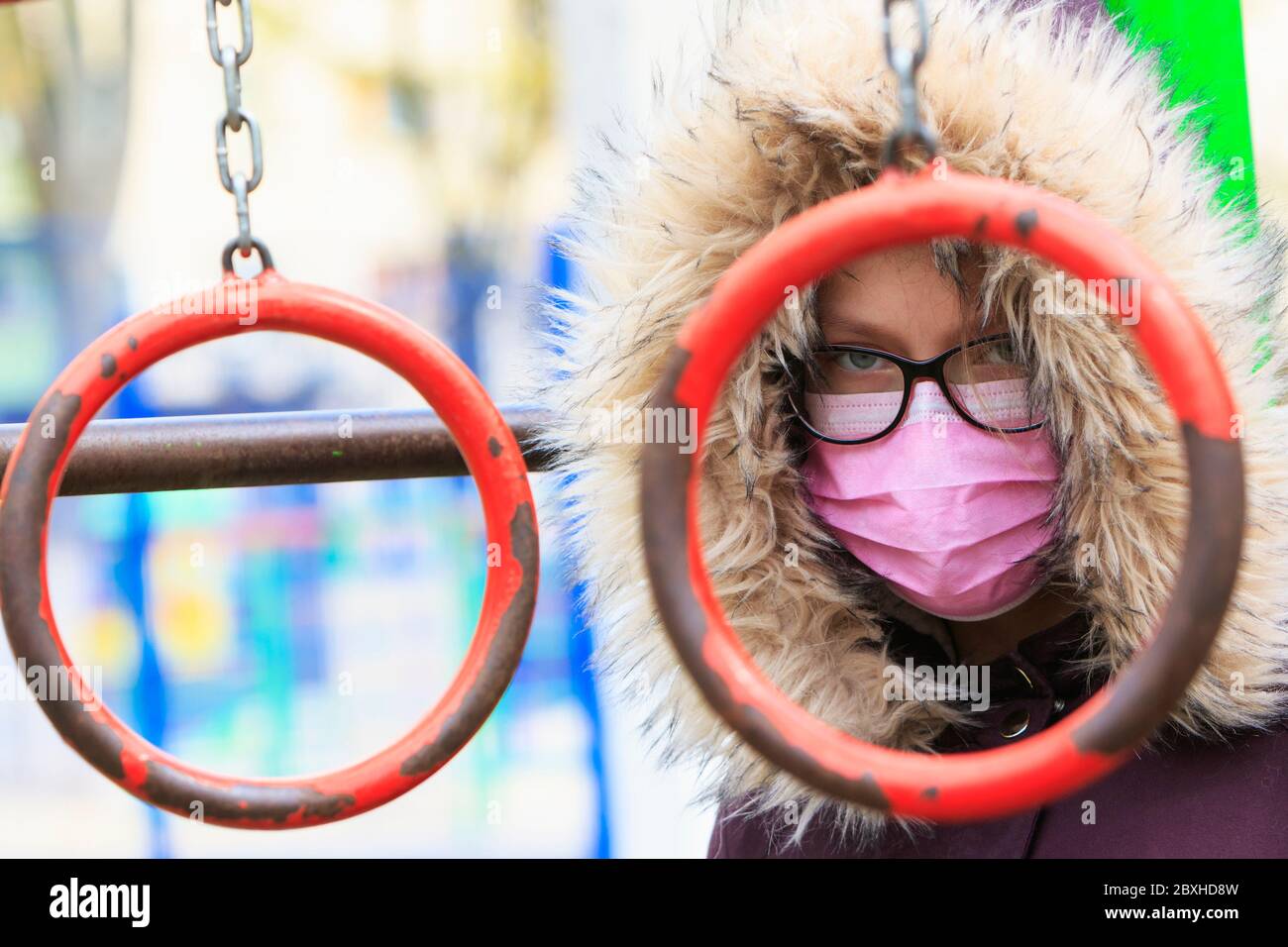 Ritratto di una ragazza in maschera medica e occhiali su un parco giochi per bambini. Foto Stock