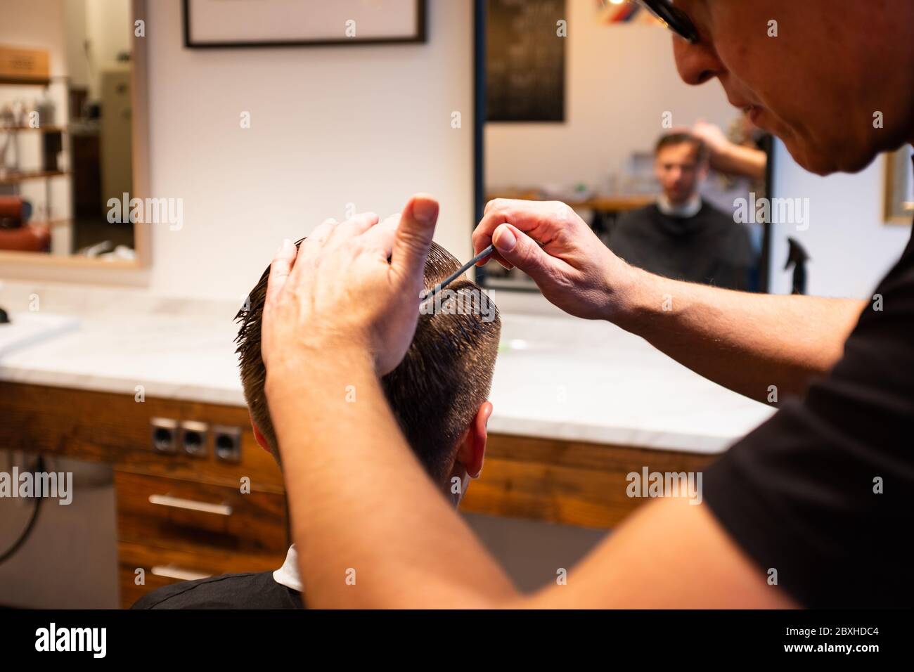 Barber sta acconciando i capelli di un giovane con un pettine nel suo barbiere, pronto a tagliare i capelli Foto Stock