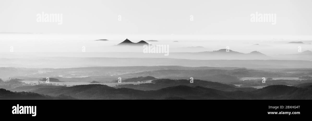 Bezdez gemelle montagne che si innalzano dalla nebbia. Inversione della temperatura meteo, Repubblica Ceca. Immagine in bianco e nero. Foto Stock