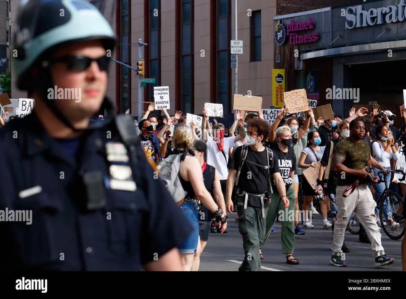 New York, New York. 6 giugno 2020. Persone che hanno segni, alcuni che tengono le mani in su in una posizione 'mani su non sparare' a una Black Lives materia solidarietà marcia attraverso Manhattan chiedendo giustizia in una serie recente di assassini della polizia americana: George Floyd, Breonna Taylor, e a innumerevoli altri. Migliaia di persone si sono unite alla marcia di protesta da Brooklyn che paralizzava Manhattan ben oltre un coprifuoco emesso all'inizio della settimana per frenare burglaries organizzati e saccheggi. Un poliziotto in un casco di rivolta cammina lungo il gruppo. 6 giugno 2020 Foto Stock