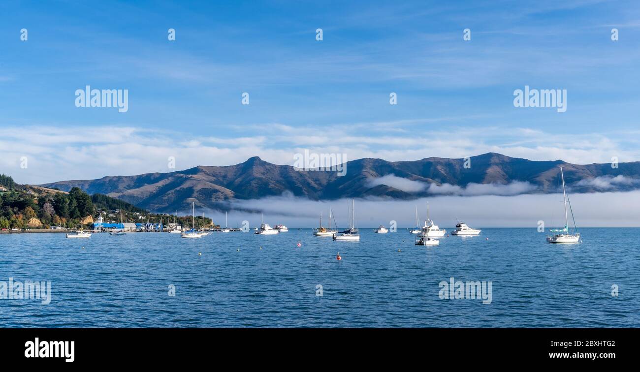 Cielo blu, nuvole bianche, mari nebulosi e acquamarini al porto di Akaroa. Ancorati sono barche da pesca e barche a vela, lungo il porto di Akaroa, Canterbury, Nuova Zea Foto Stock