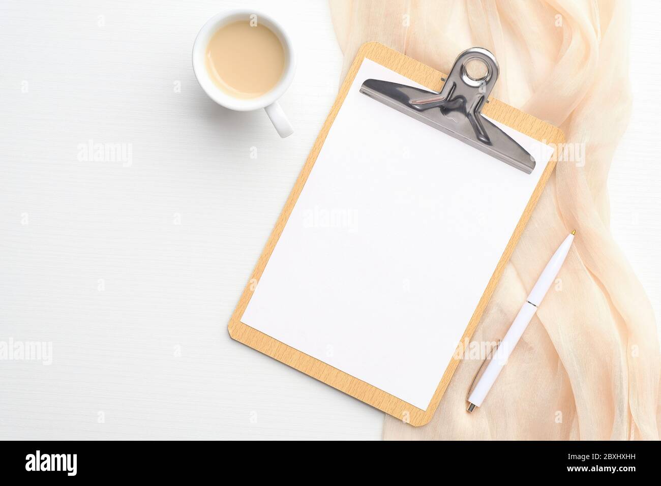 Spazio di lavoro femminile con appunti con nota di carta vuota, tazza di caffè, sciarpa beige e penna su sfondo bianco. Pianificatore di nozze, lista di controllo, per fare lis Foto Stock