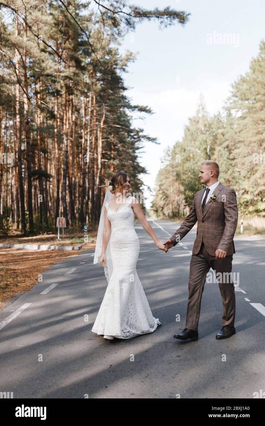 Sposa e sposo che si dirigono sulla strada nella foresta tenendolo le mani l'un l'altro. Ritratto di sposa e sposo Foto Stock