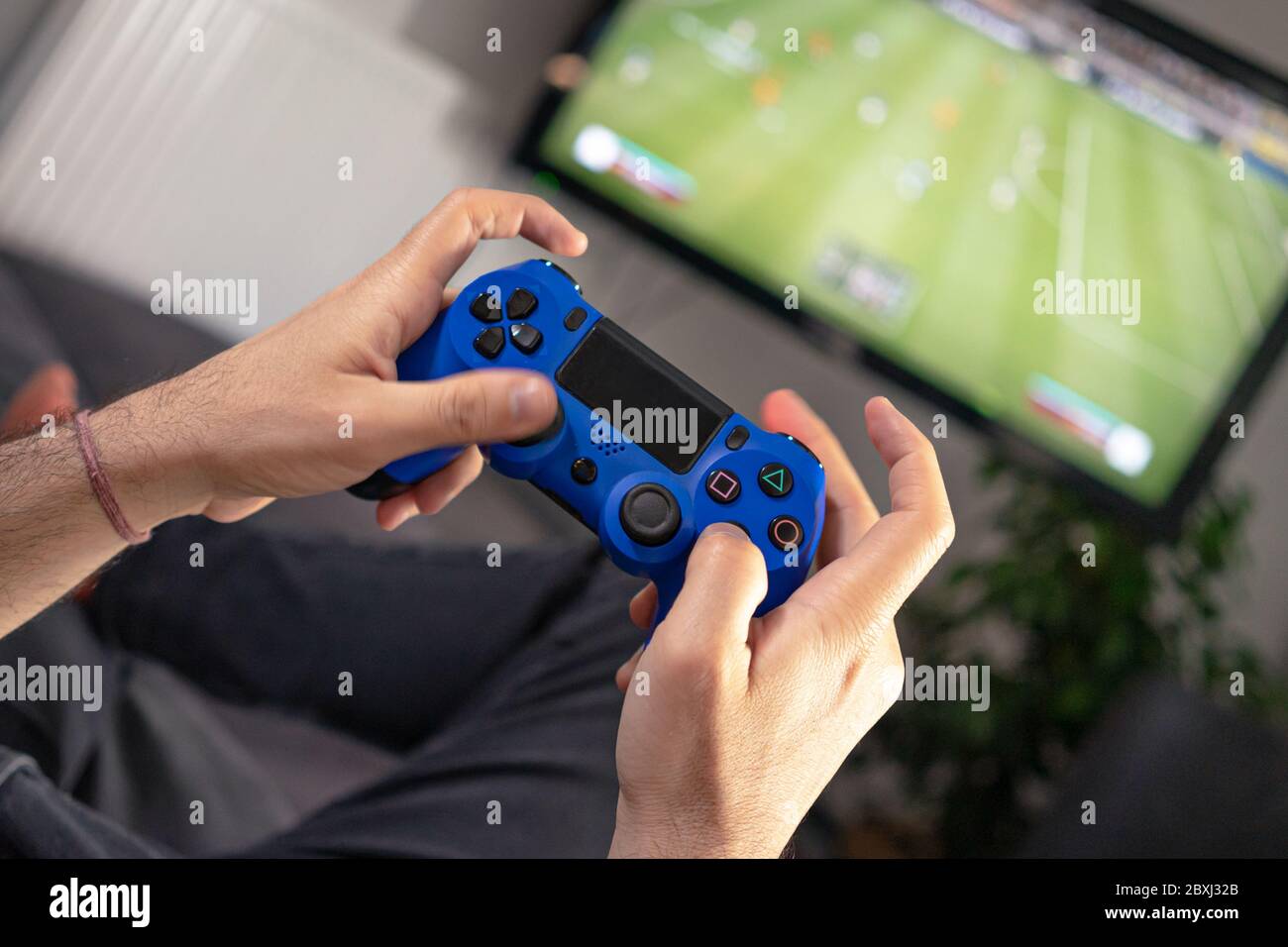 mani dell'uomo che tengono il joystick e che giocano a casa sul divano dell'autobus di fronte alla televisione con un gioco di gioco a concole Foto Stock