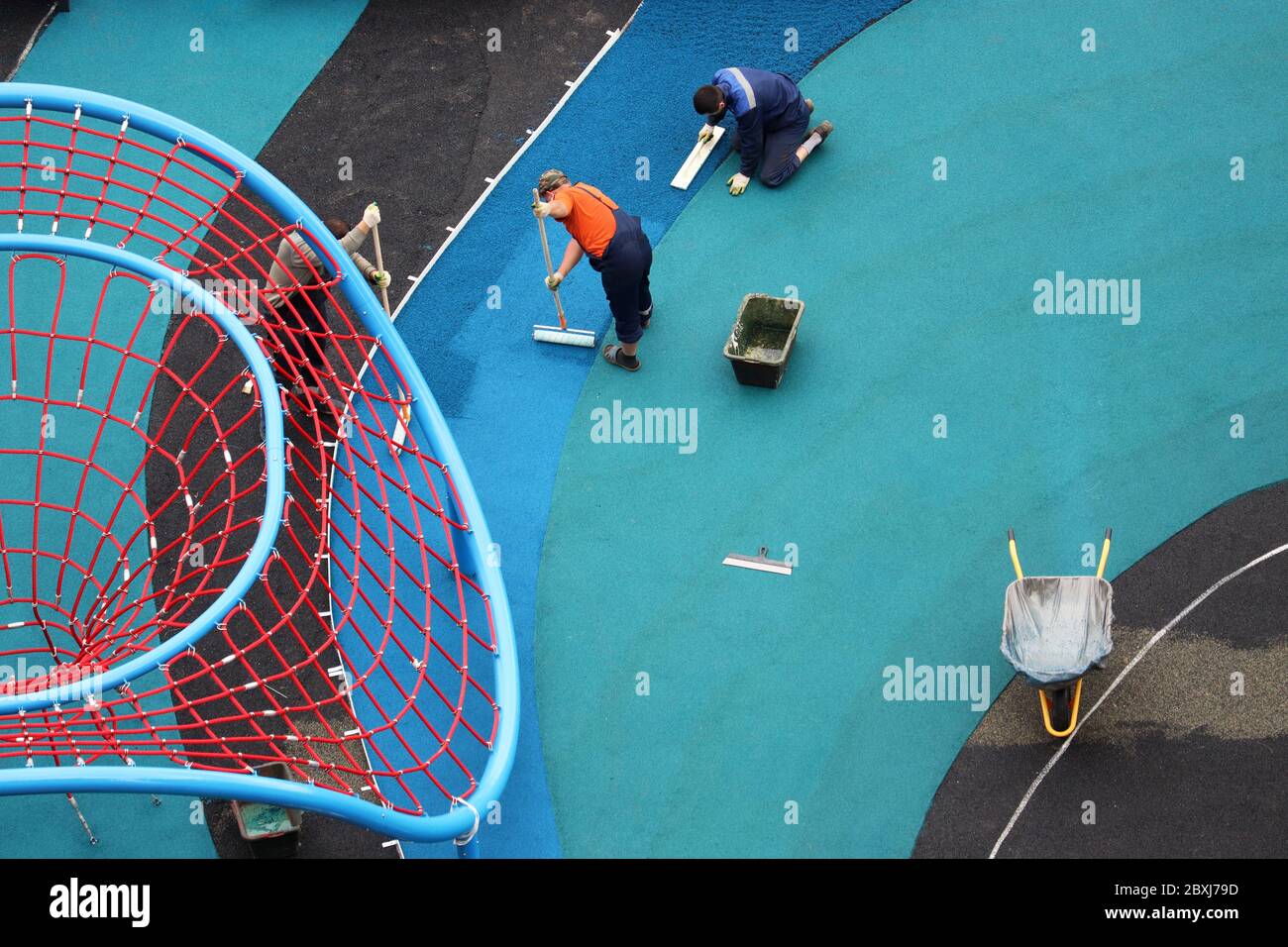 I lavoratori ricoprono il rivestimento in gomma sul parco giochi, vista dall'alto. Rivestimento morbido per la sicurezza dei bambini Foto Stock