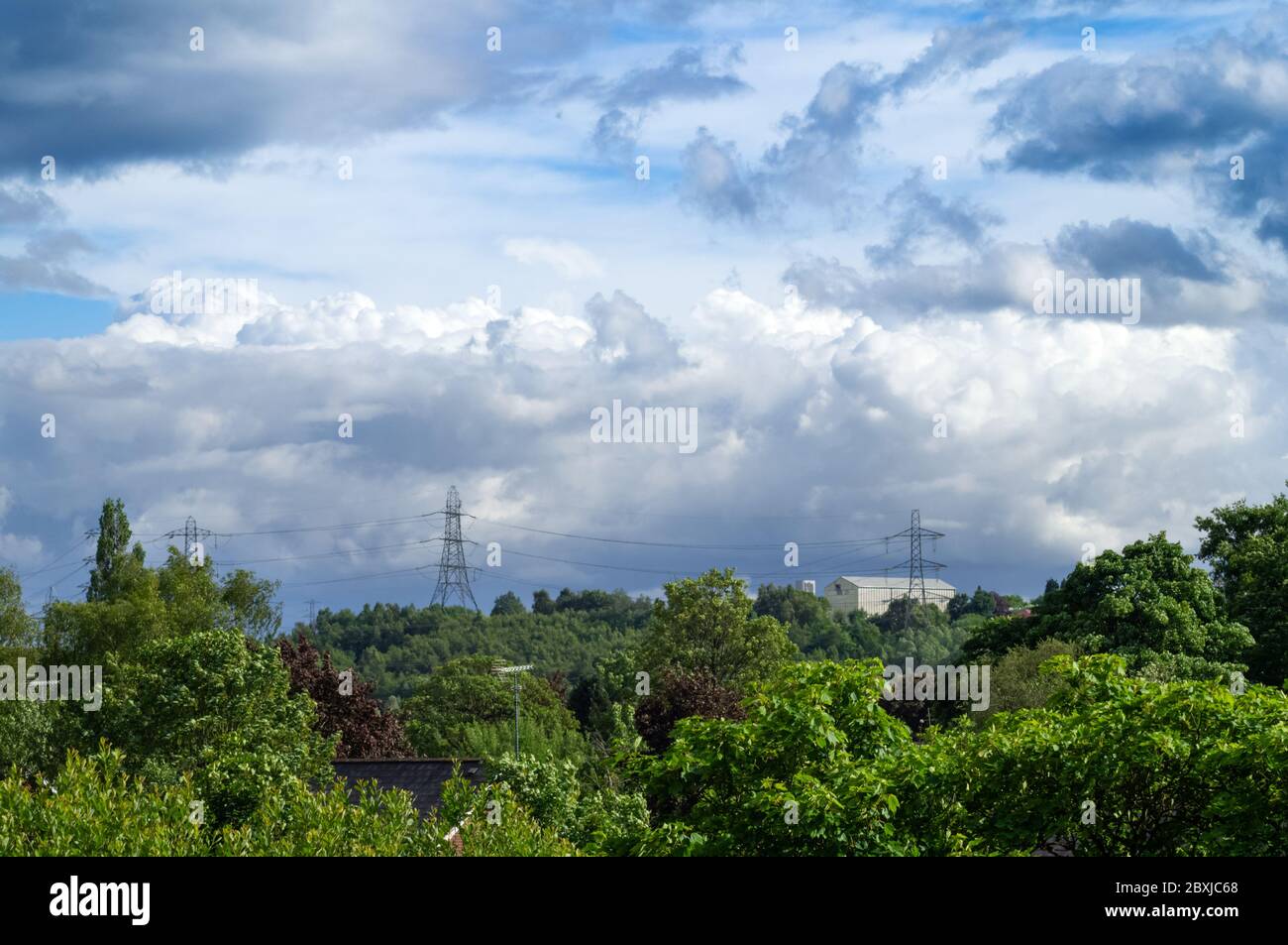 Cielo di Moody con le nuvole di pioggia tempesta nuvole sopra due tralicci e cespugli verdi alberi arbusti paesaggio urbano Foto Stock