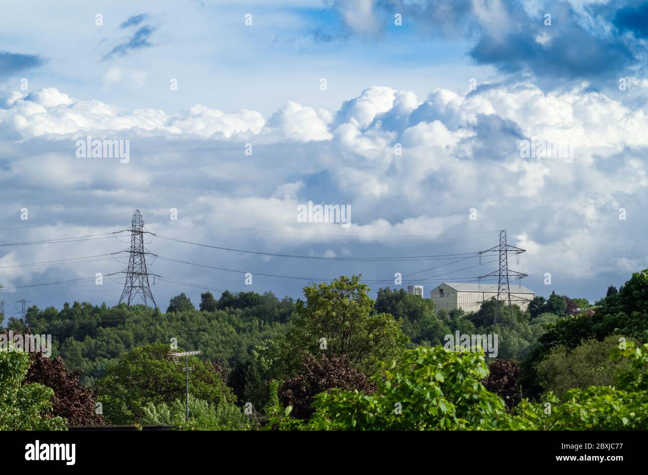Cielo di Moody con le nuvole di pioggia tempesta nuvole sopra due tralicci e cespugli verdi alberi arbusti paesaggio urbano Foto Stock