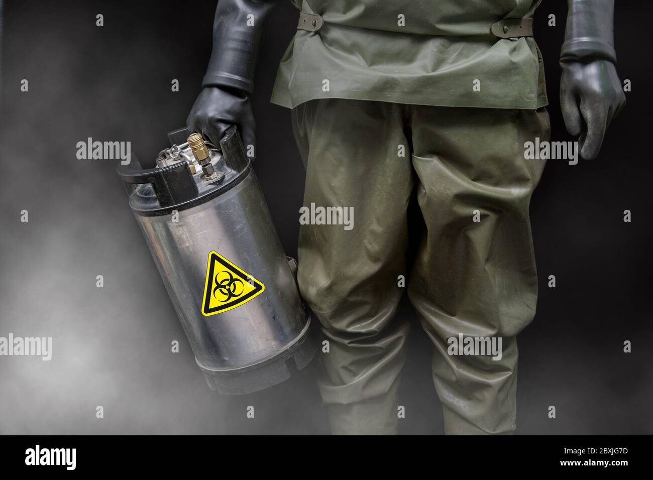 Un uomo in una tuta protettiva completa NBC tiene in mano uno speciale contenitore metallico con un adesivo di avvertenza di rischio biologico. Foto Stock