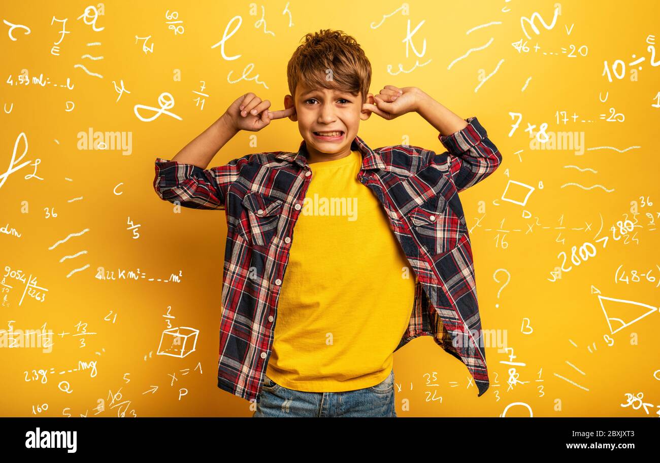 Bambino copre le orecchie perché non vuole sentire spiegazioni di matematica. Sfondo giallo Foto Stock