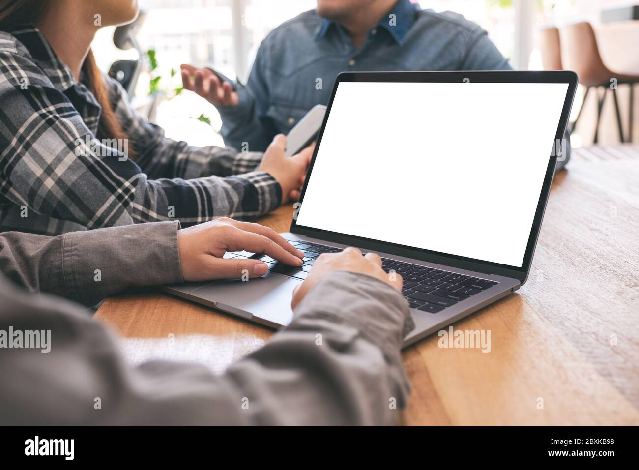 Una donna che usa e digita un computer portatile mockup con amici in background Foto Stock