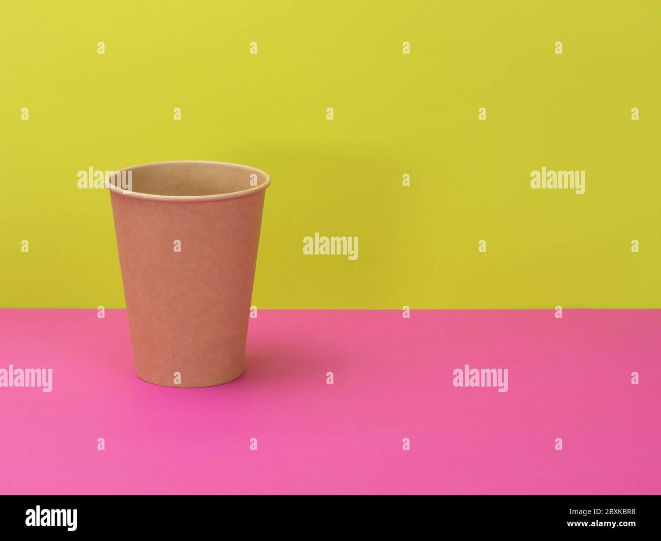Tazza di carta monouso su sfondo rosa e verde. Foto Stock
