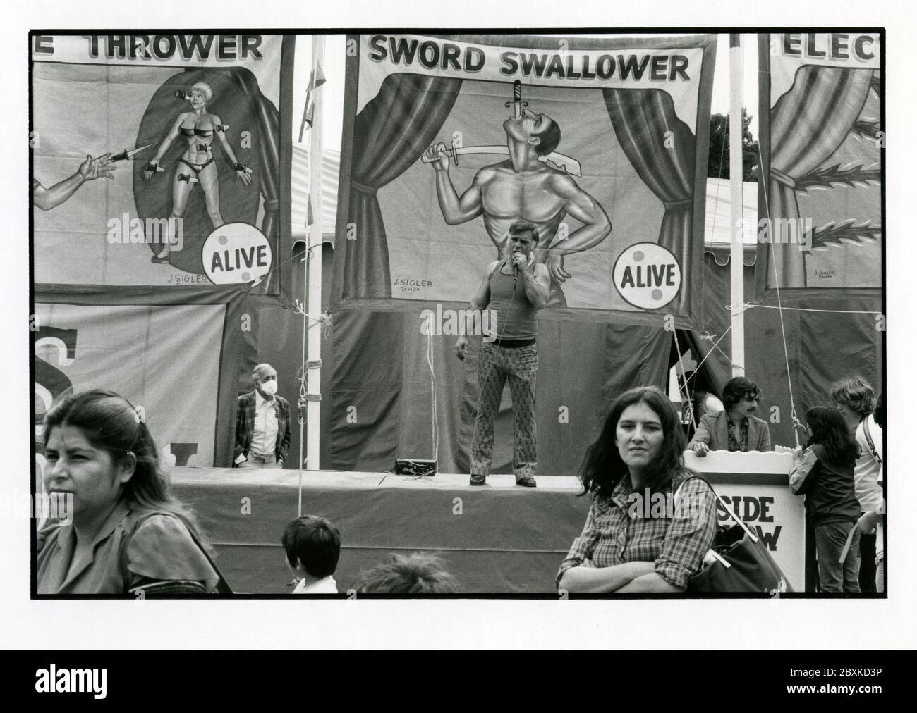 Old Time circus carny con le indicazioni dipinte a mano per le attrazioni laterali e le persone che partecipano a Hollywood, CA circa anni '70 Foto Stock