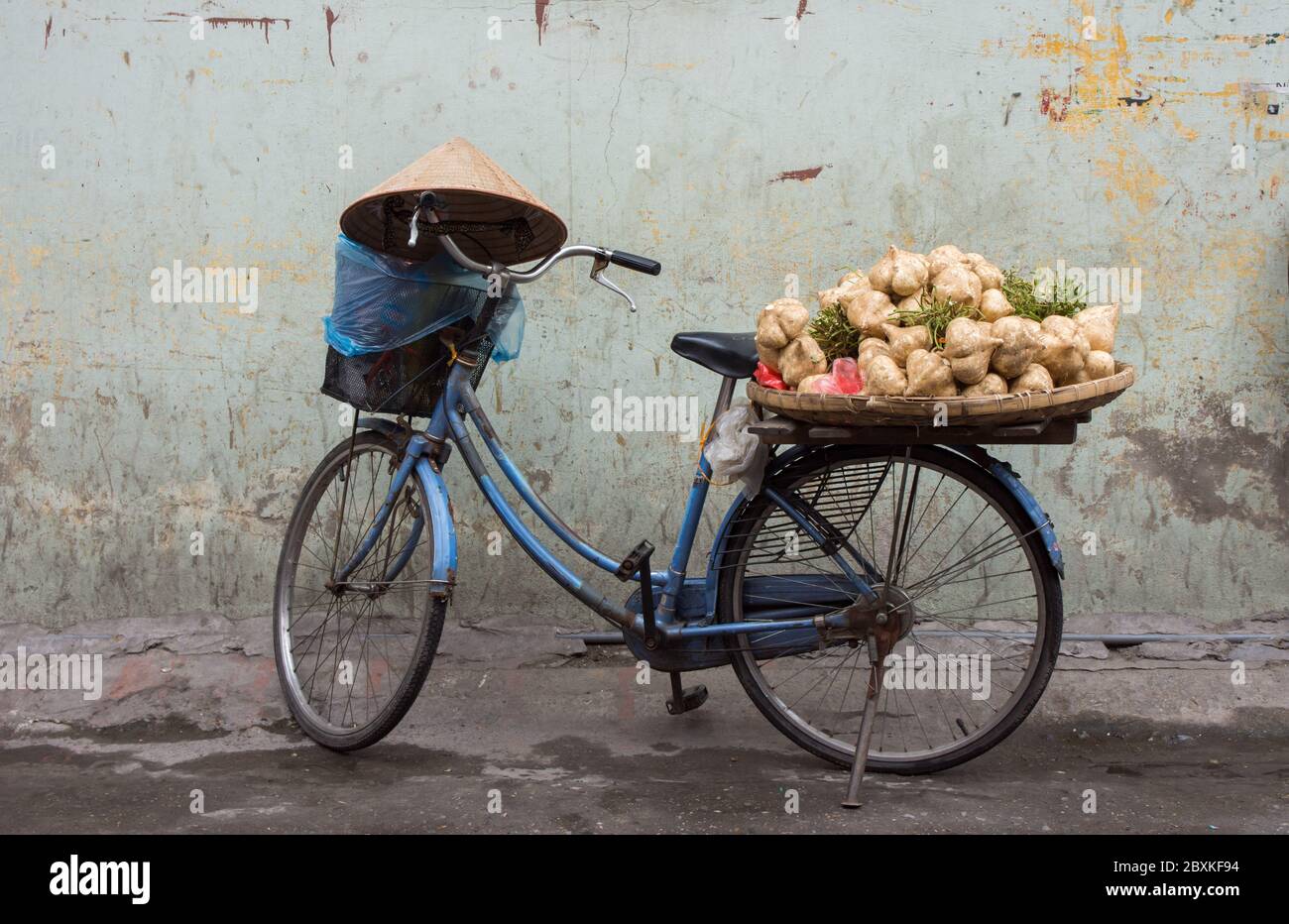 Carico tradizionale vietnamita di bicicletta con verdure e cappello conico poggiato sul manubrio. Foto Stock