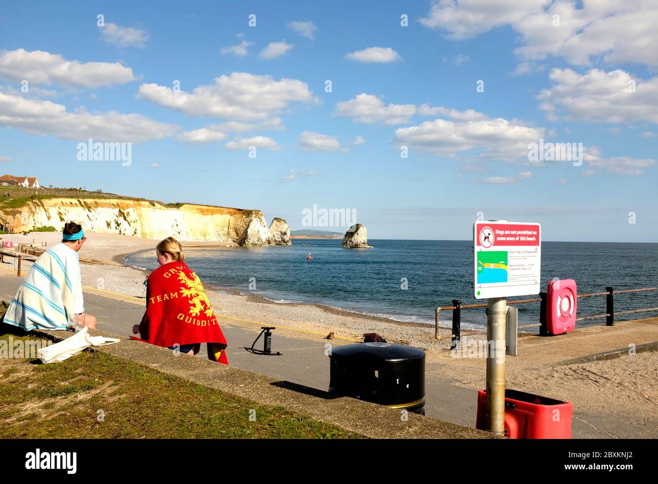 Vista di Freshwater Bay Isola di Wight due donne sedette sulla parete del lungomare con asciugamani colorati che chiacchierano con la pagaia kayak pompa aria nella baia Foto Stock