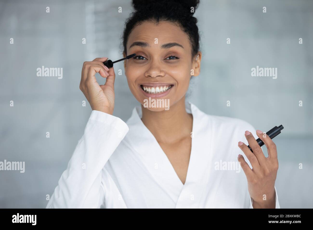 Testa ritratto girato sorridendo donna afroamericana applicando mascara nero Foto Stock