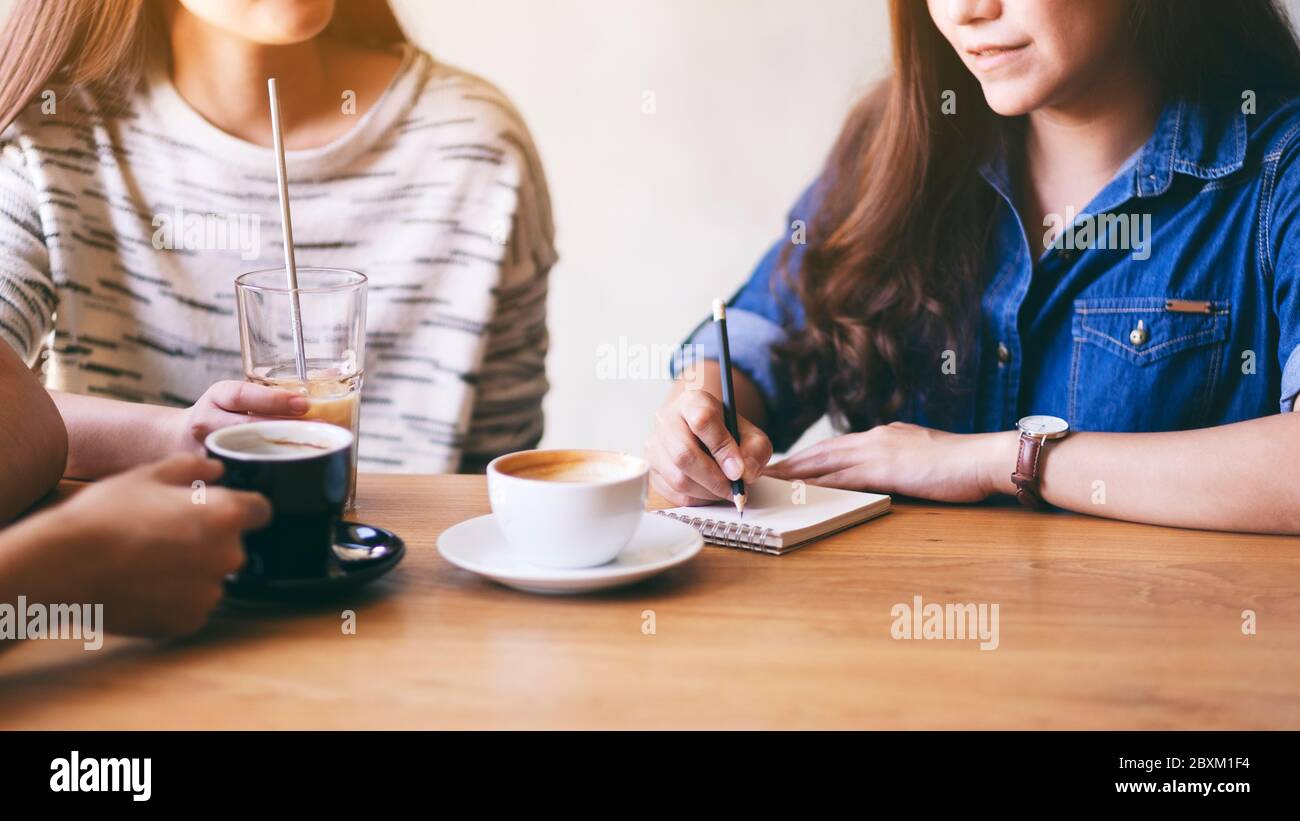 Una donna che scrive su un notebook mentre beve caffè con gli amici Foto Stock