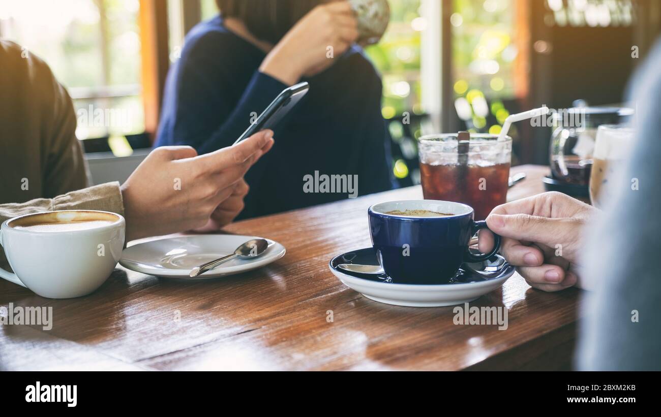 Immagine di primo piano di persone che usano il telefono cellulare e bevono caffè insieme in un caffè Foto Stock