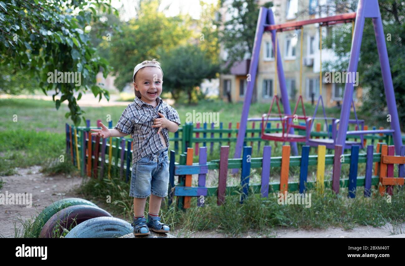Il bambino sta mostrando emozioni. Il bambino ride, sorride, mostra gesti, mostra una mano. Il bambino gioca nel parco giochi. Foto Stock