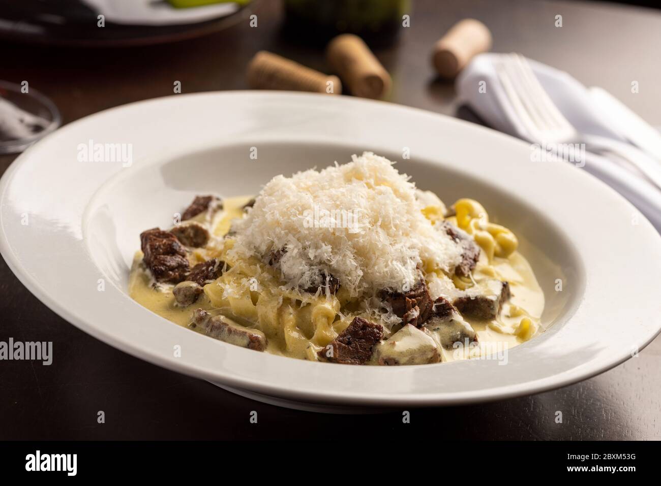 gnocchi di carne e formaggio preparati con un sifone e una salsa cremosa bianca su vino da tavola, bicchiere, tappi e tovaglioli Foto Stock