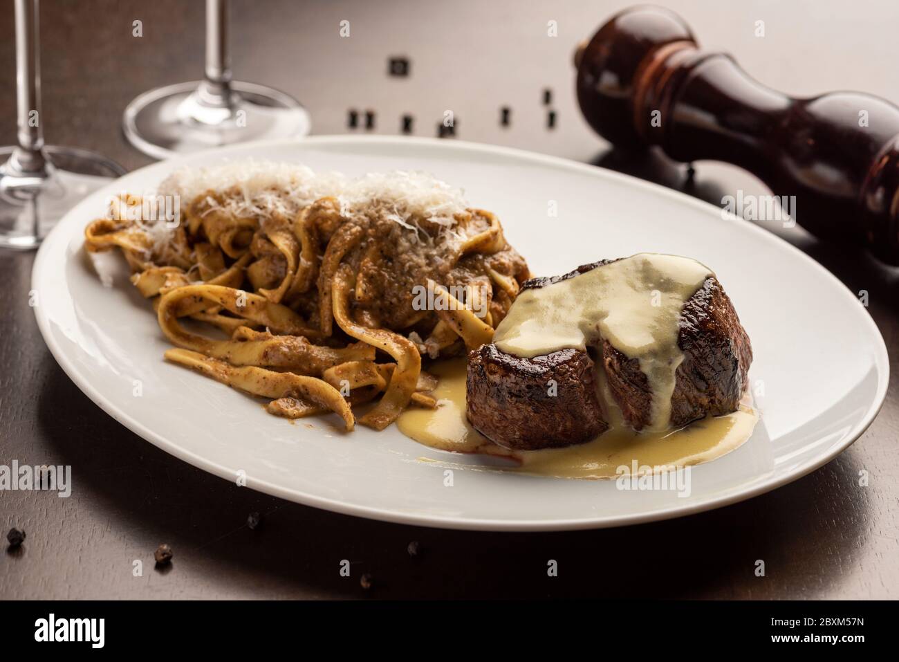 filetto di manzo con salsa e tagliatelle su tavola di legno con pepai e bicchiere di vino Foto Stock