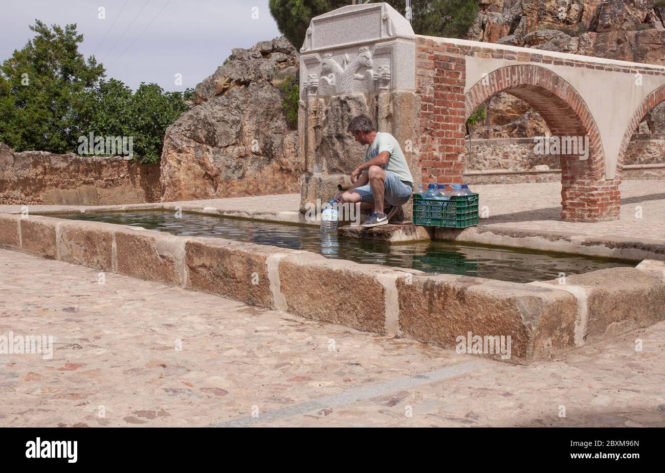 Uomo residente imbottigliare le bottiglie alla fontana Palomas Pillar costruita nel 16 ° secolo, Hornachos, Spagna. Stemma imperiale di a. Foto Stock
