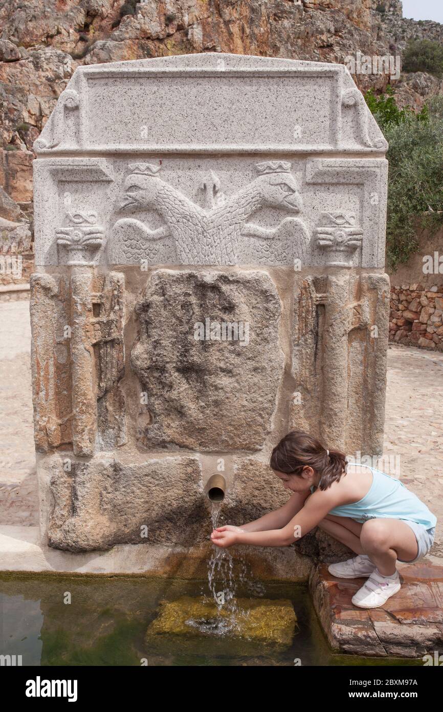 Bambina che beve sulle mani alla fontana del Palomas Pillar, Hornachos, Spagna. Stemma imperiale di Carlos V scolpito al centro Foto Stock