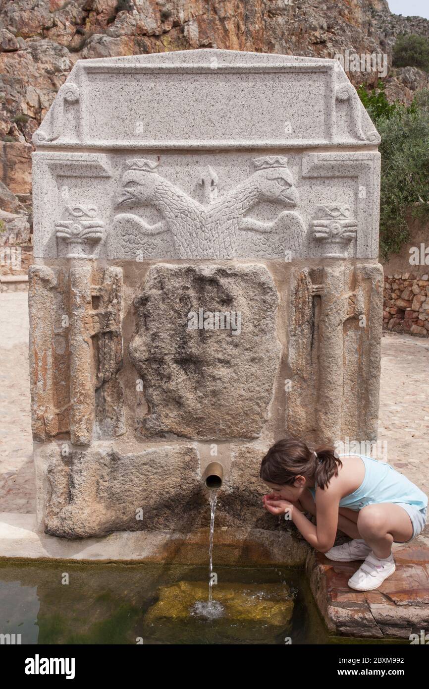 Bambina che beve sulle mani alla fontana del Palomas Pillar, Hornachos, Spagna. Stemma imperiale di Carlos V scolpito al centro Foto Stock