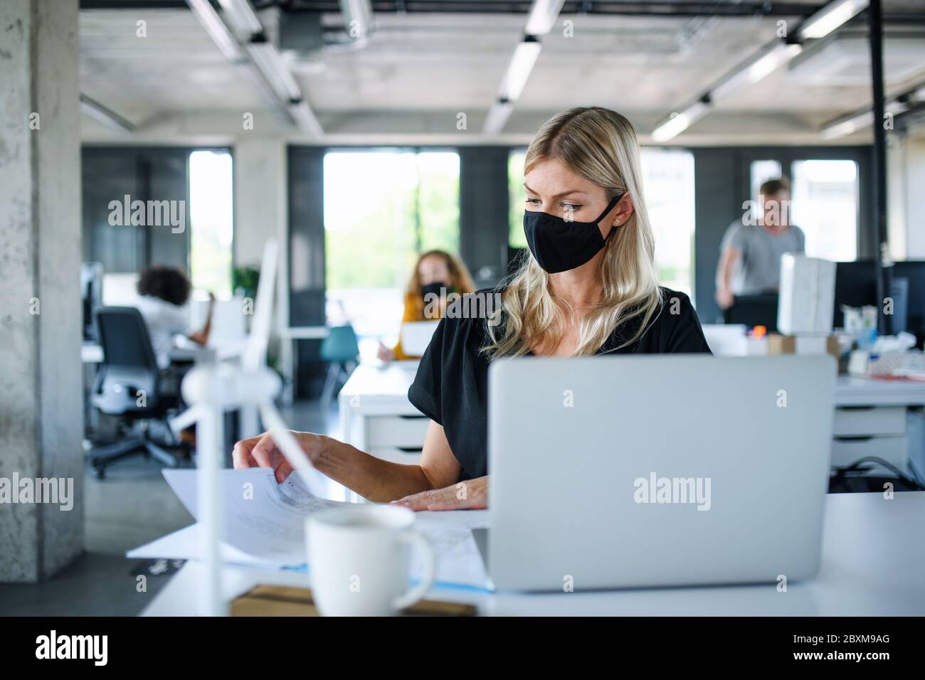 Giovane donna con maschera di protezione al lavoro in ufficio dopo il blocco, lavorando. Foto Stock