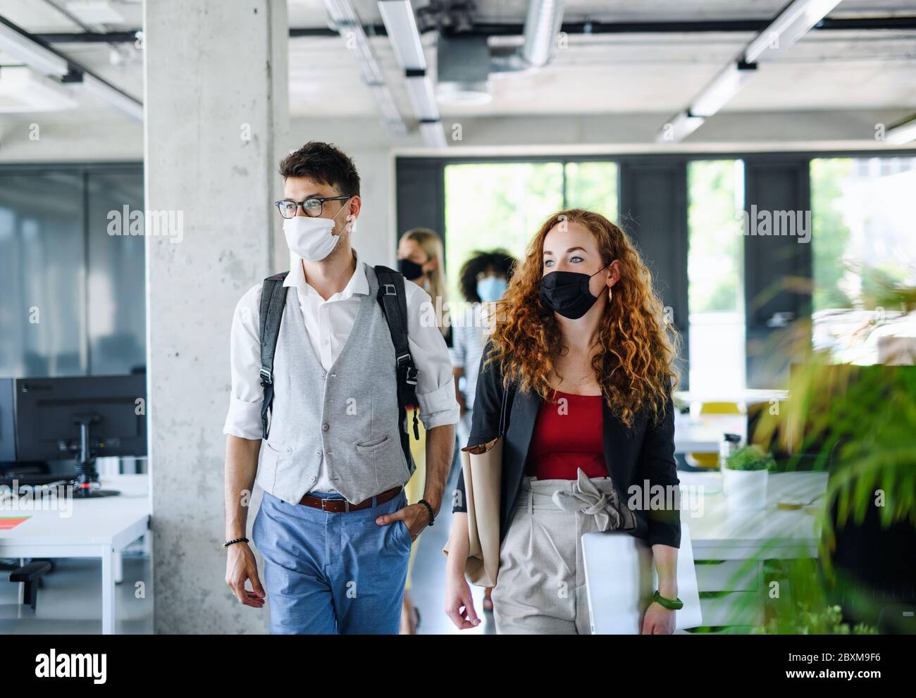 Giovani con maschere di fronte al lavoro in ufficio dopo blocco, a piedi. Foto Stock