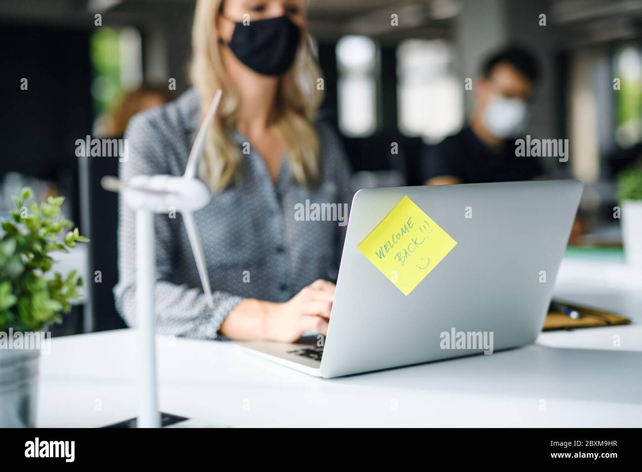 Giovane donna irriconoscibile con maschera facciale di nuovo al lavoro in ufficio dopo il blocco. Foto Stock