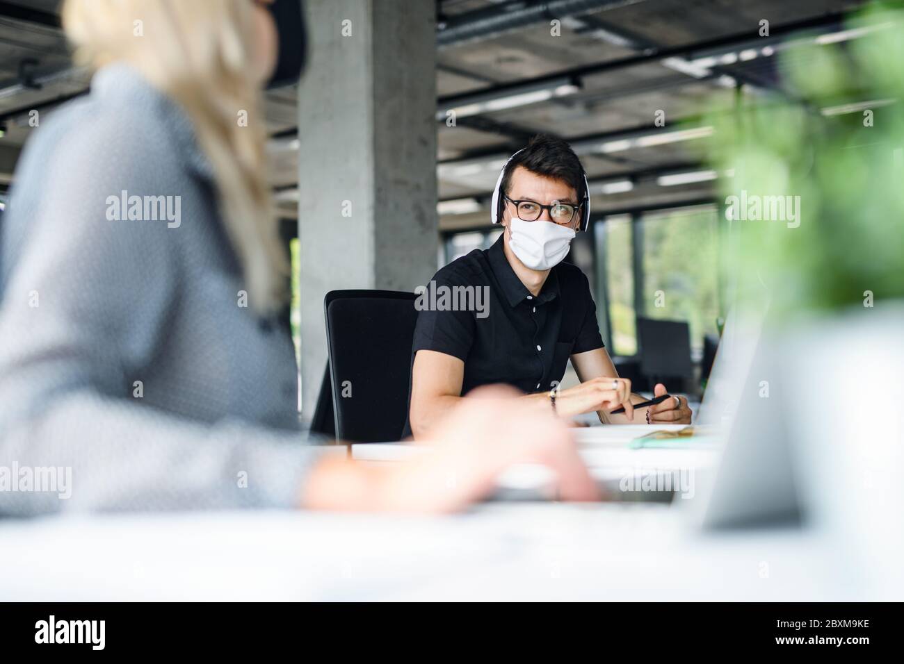 Giovani con maschere di fronte al lavoro in ufficio dopo blocco, parlando. Foto Stock