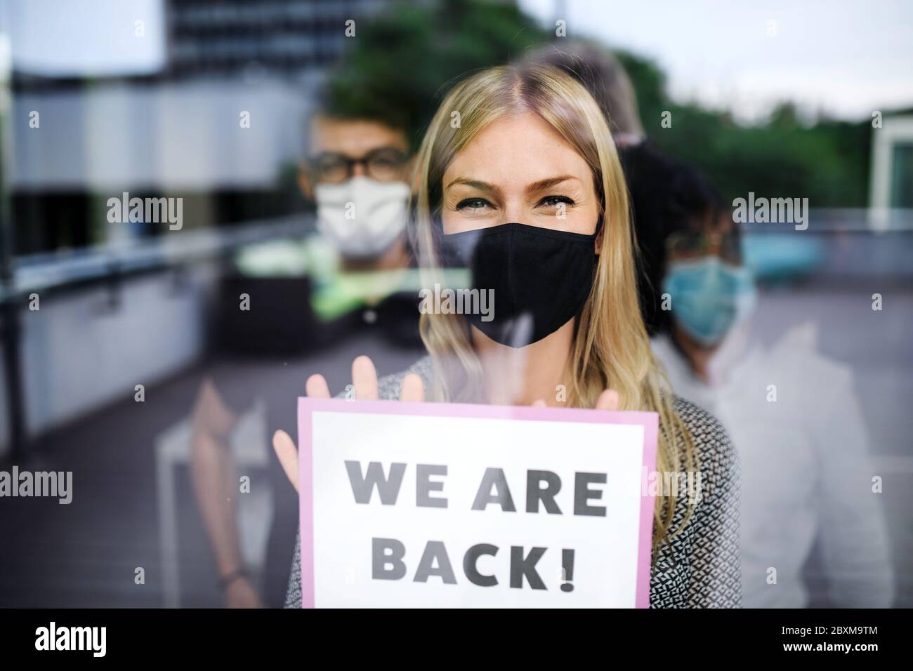 Donna con maschera di protezione indietro al lavoro in ufficio dopo il blocco, tenendo siamo indietro segno. Foto Stock