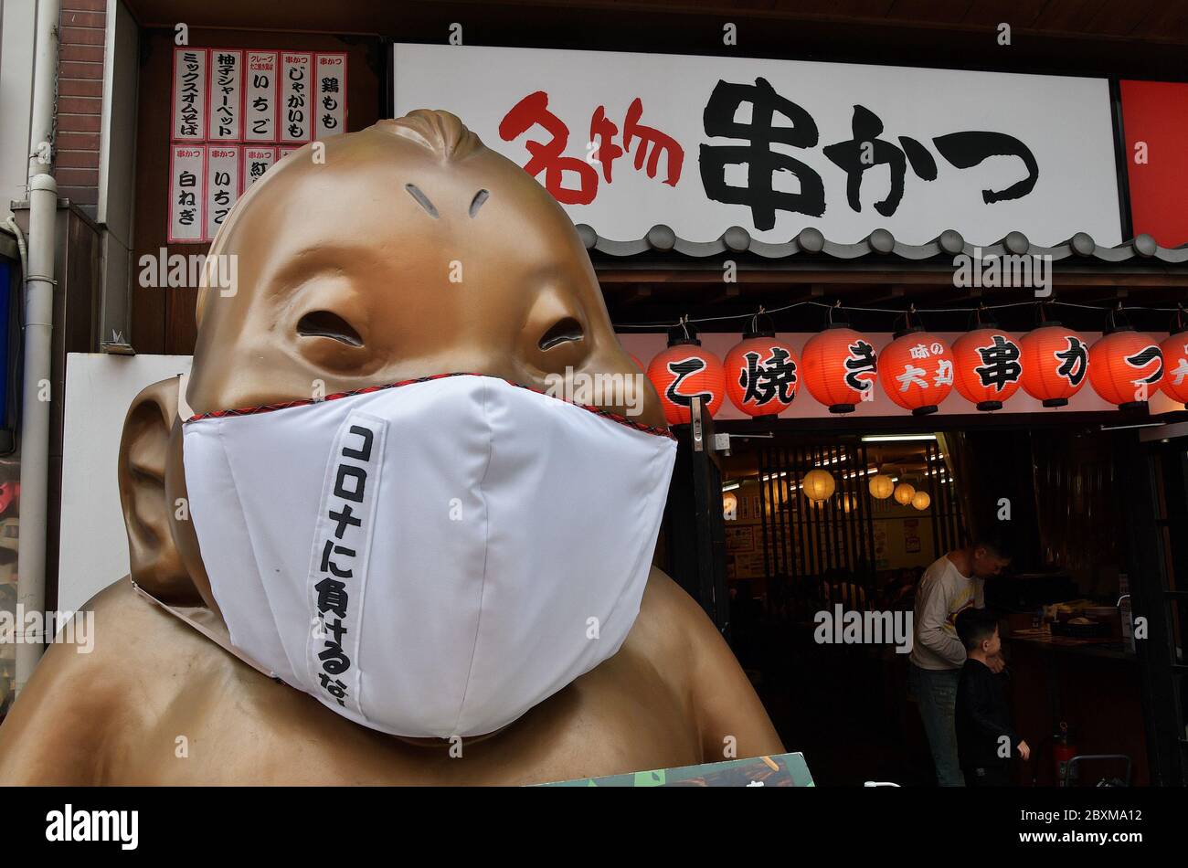 La statua di Billiken che indossa maschere facciali è vista al quartiere dello shopping e del divertimento di Shinsekai a Osaka, Japn il 6 giugno 2020. Foto Stock