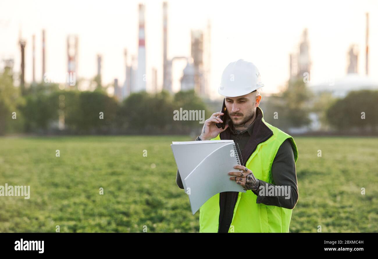 Giovane ingegnere con smartphone in piedi all'aperto da raffineria di petrolio. Spazio di copia. Foto Stock