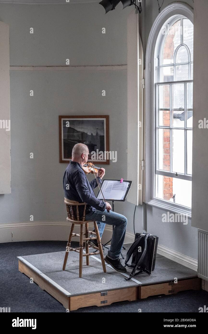 Nella città di Presteigne in Galles, Regno Unito, il musicista John Hymas intrattiene i clienti in fila pazientemente fuori dai negozi nella strada alta durante la chiusura Foto Stock