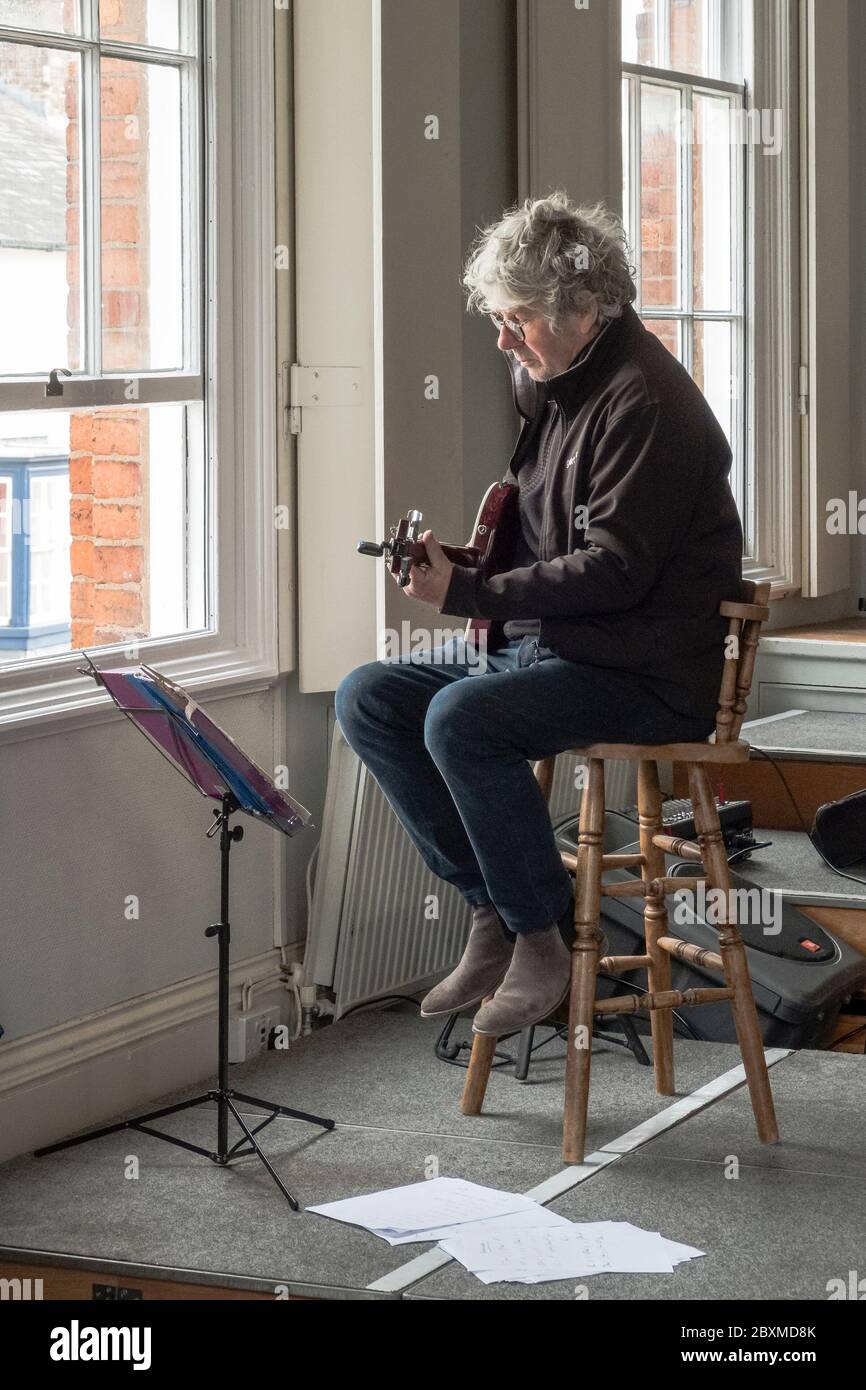 Nella città di Presteigne in Galles, Regno Unito, il musicista Pete Mustil intrattiene i clienti in fila pazientemente fuori dai negozi nella strada alta durante la chiusura Foto Stock
