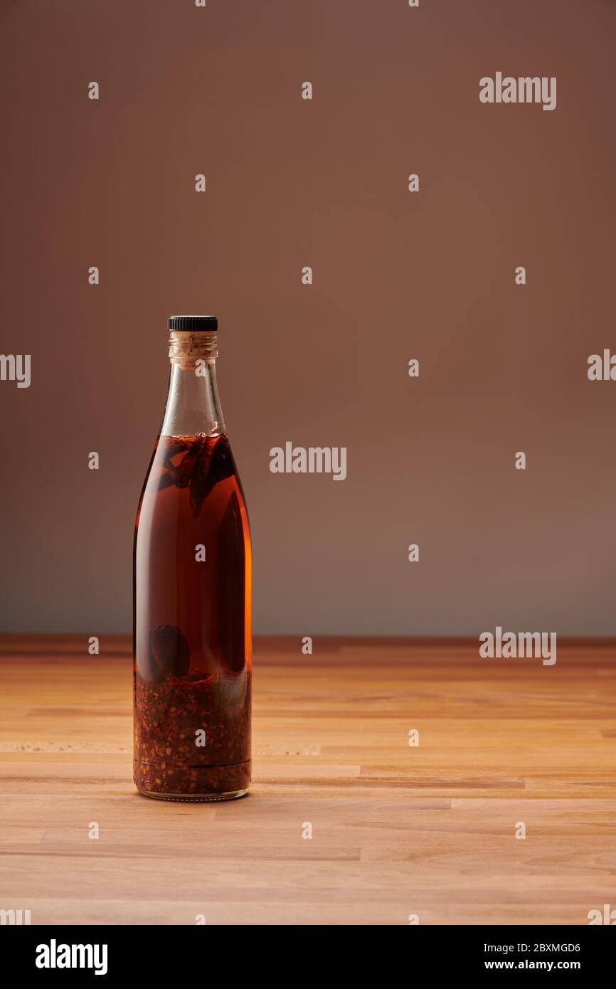 Bottiglia trasparente di olio di peperoncino fatto in casa con pezzi di peperoncino secco, su un tavolo di legno Foto Stock