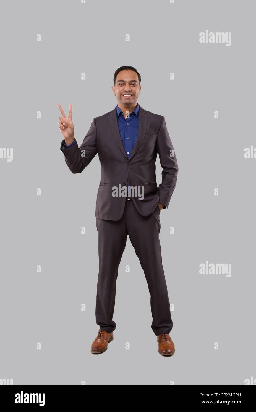 Uomo d'affari che mostra il segno di pace. Indio uomo d'affari in piedi di lunghezza completa. Foto Stock