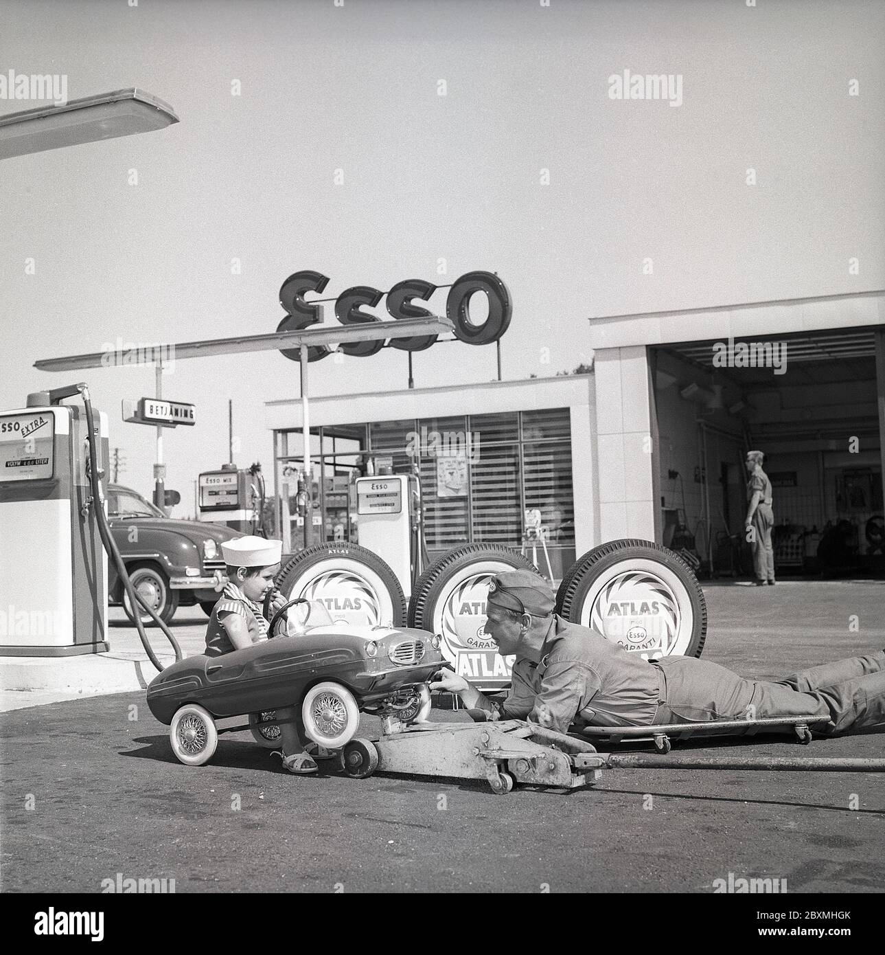 Stazione di servizio degli anni '50. Un ragazzo nella sua pedalò lo ha  servito in un distributore di benzina esso. Un addetto alla manutenzione ha  sollevato la piccola auto e la sta