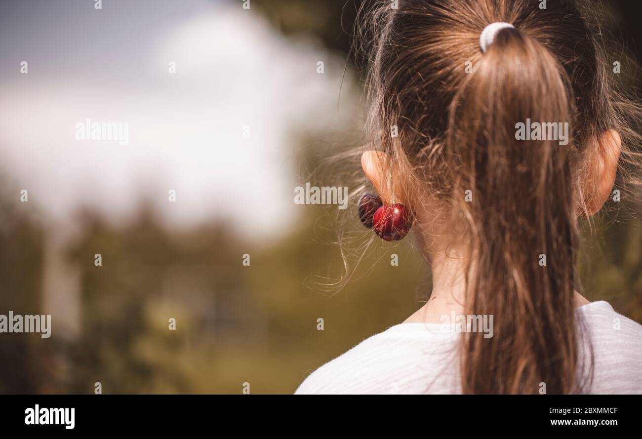 La bambina ha avuto una ciliegia fresca sull'orecchio. Fare gioielli da frutta. Adorabile bambina con una ciliegia sull'orecchio. Foto Stock