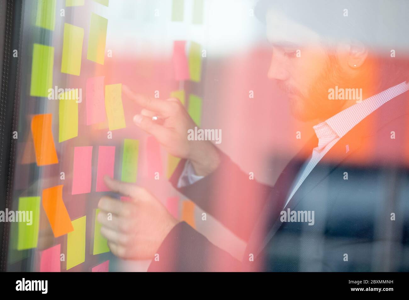 Visualizza attraverso l'imprenditore della finestra scrivendo idee di avvio su note appiccicose Foto Stock
