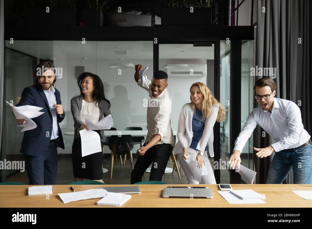Il personale diversificato balla in giro sul posto di lavoro celebrando la vittoria Foto Stock