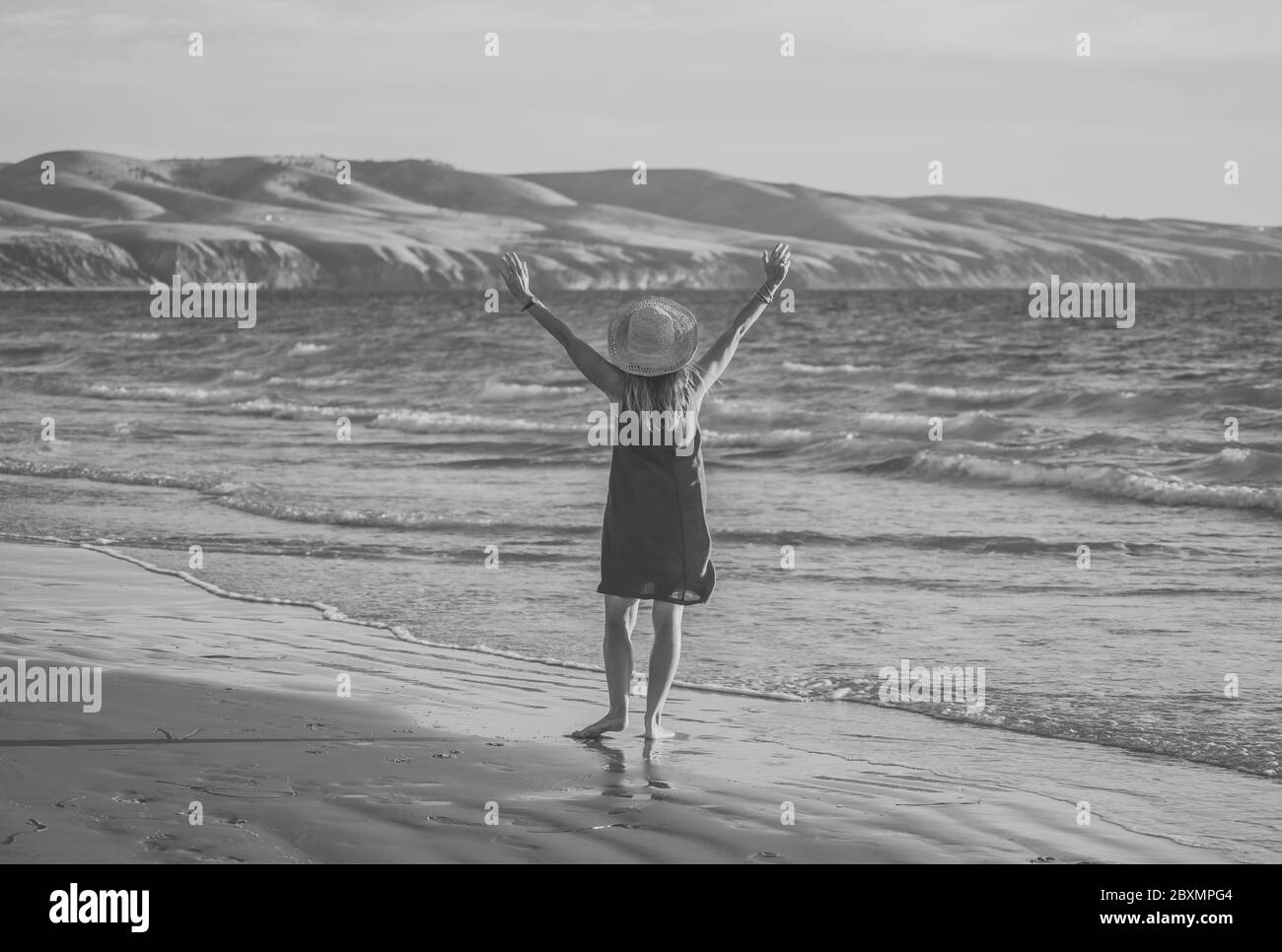 Felice attraente donna matura in abito rosso godendo all'aperto e la libertà sulla spiaggia, braccia aperte in tensione nella speranza dopo la quarantena di coronavirus eas Foto Stock