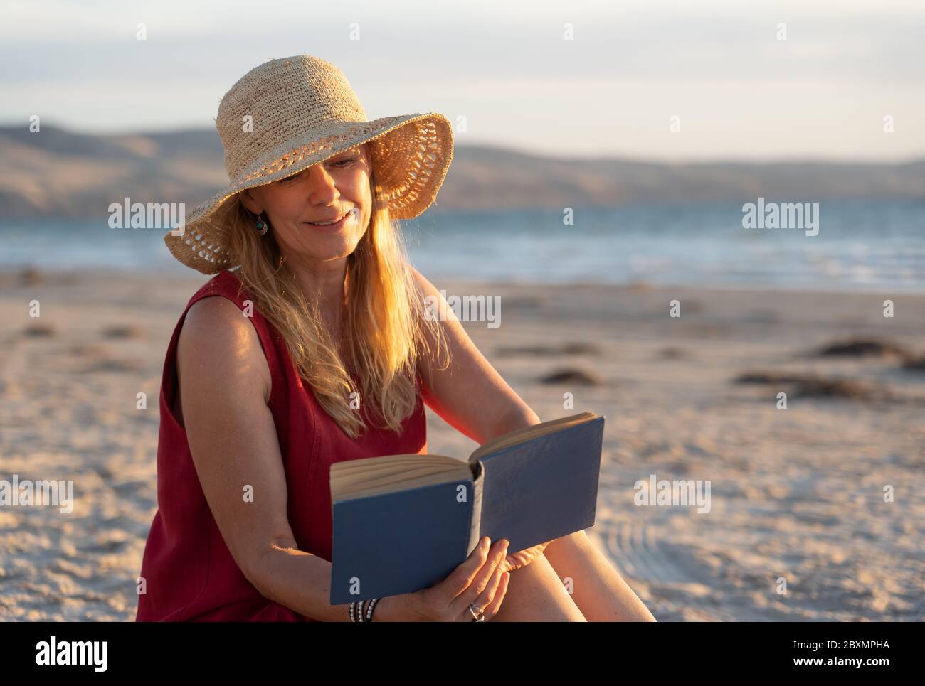 Felice attraente donna matura in abito rosso godendo all'aperto e la libertà sulla spiaggia, braccia aperte in tensione nella speranza dopo la quarantena di coronavirus eas Foto Stock