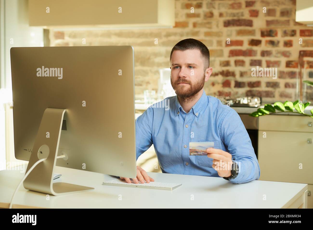 Un uomo con la barba si siede davanti al computer e digita le informazioni della carta di credito in un negozio online a casa. Un ragazzo che fa un pagamento online sul Foto Stock