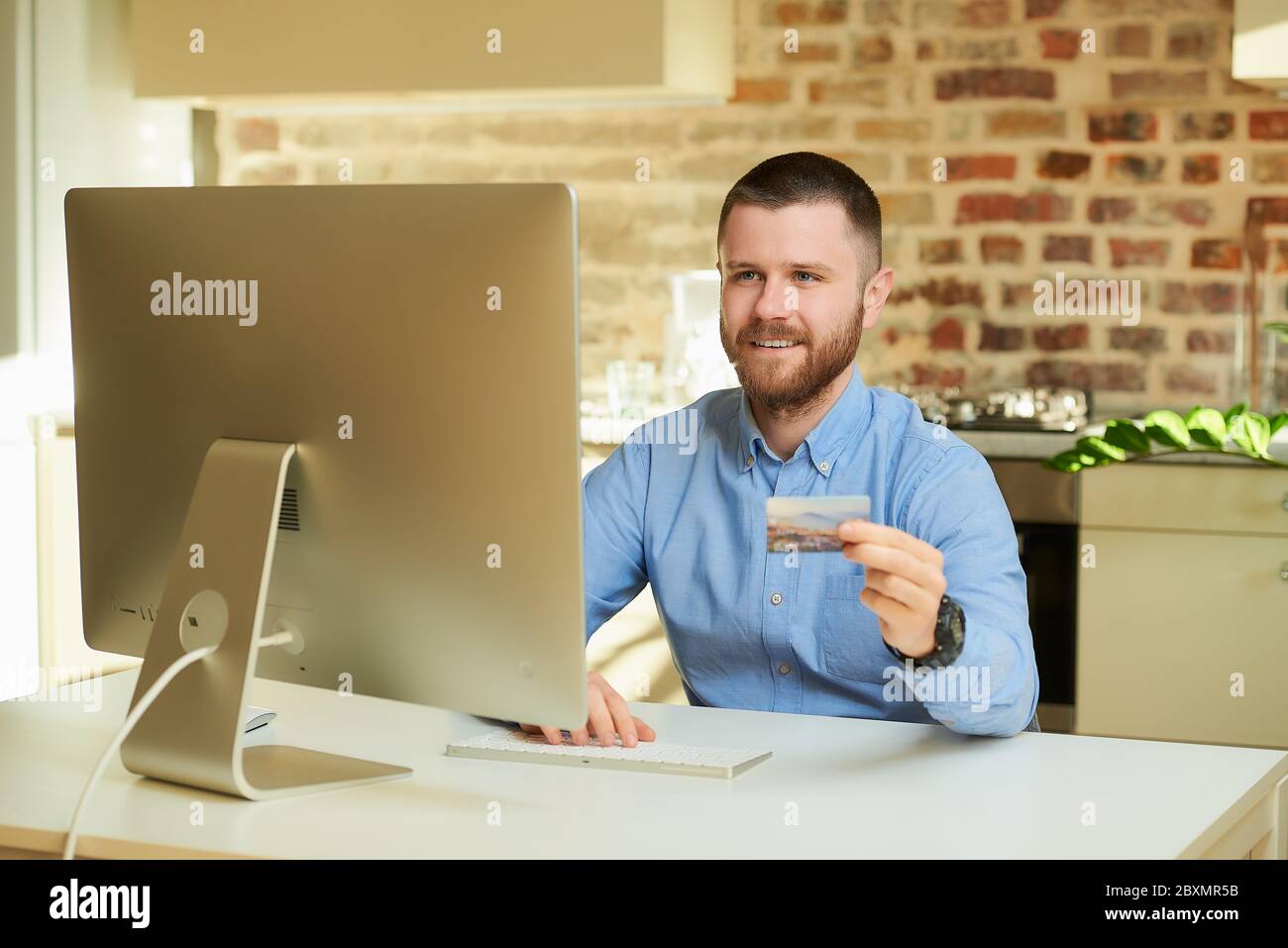 Un uomo felice si siede davanti al computer e digita le informazioni sulla carta di credito in un negozio online a casa. Un ragazzo che fa un pagamento online sul internee Foto Stock