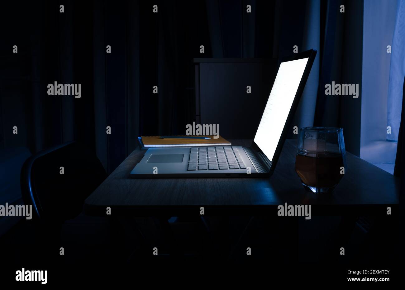 WFH - lavorare fuori orario e lavorare da casa a tarda notte su un notebook con blocco note e bicchiere di whisky 1 Foto Stock