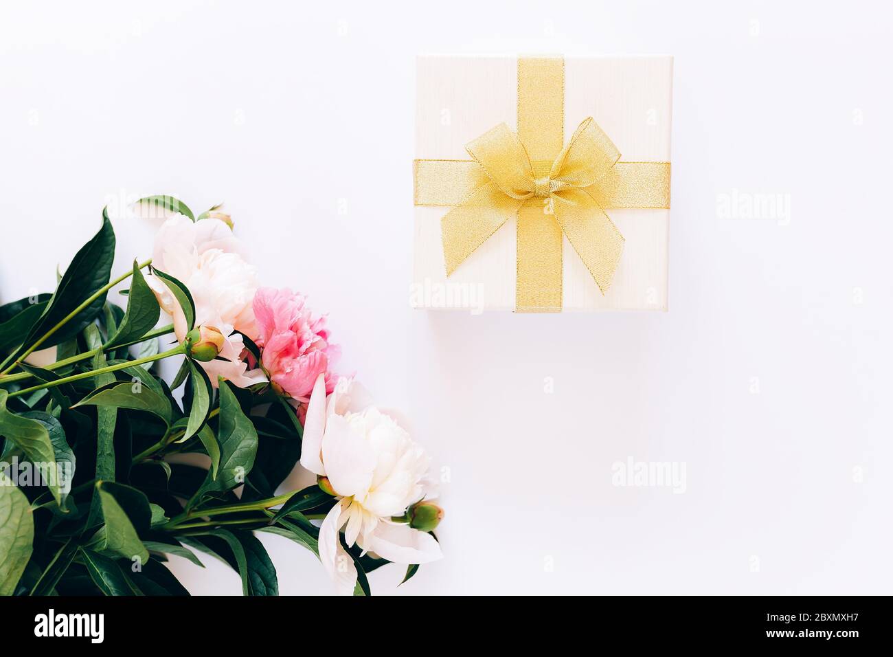 Bel bouquet di peonie e una scatola bianca con un arco giallo su sfondo bianco, peonie fiorite Foto Stock